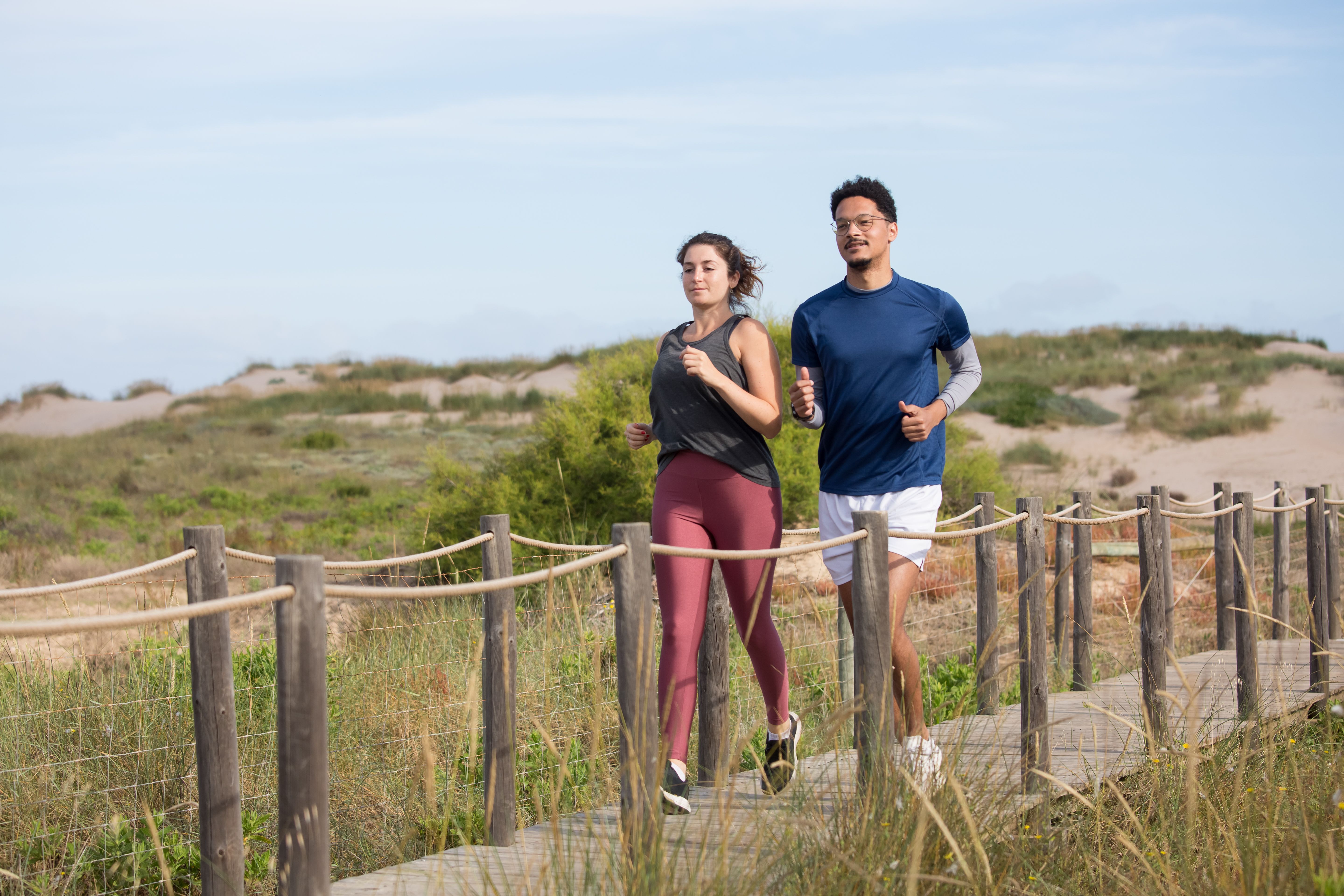 A man and a woman running together on a coastal boardwalk